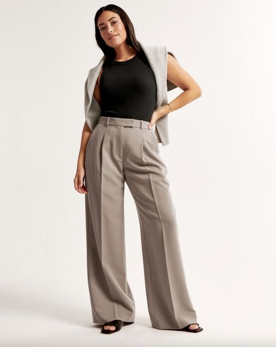 A woman strikes a pose in a sleeveless top, wide-legged trousers, and a flowing vest.