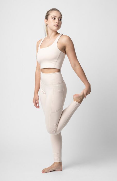 A model wearing white leggings paired with a matching sports bra, holding one leg in a stretch pose