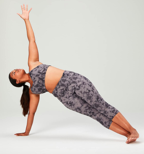 A model wears black tie-dye printed crop leggings while holding a side plank position.