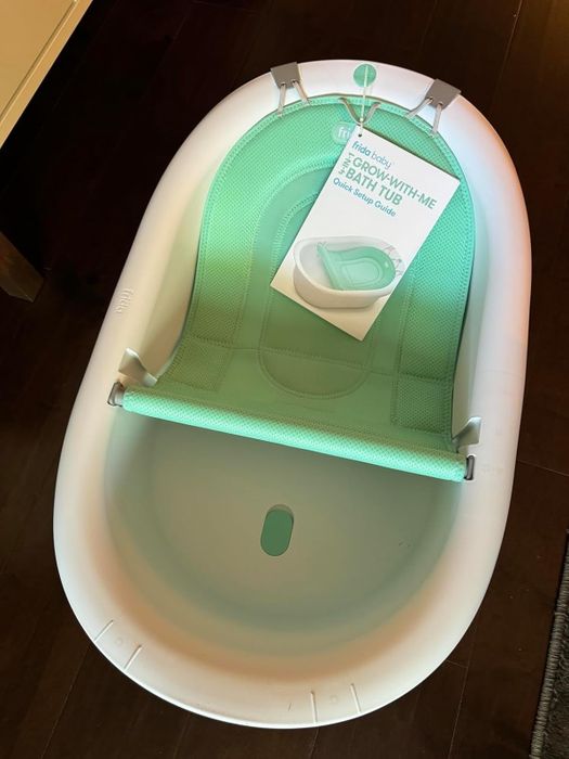 Frida Baby 4-in-1 Sling 'n Seat Bath Tub, featuring a green mesh support sling and an included Quick Setup Guide for easy installation.