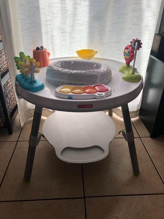 An interactive children's activity table features a variety of toys, including a tree, piano keys, and a spinning toy.