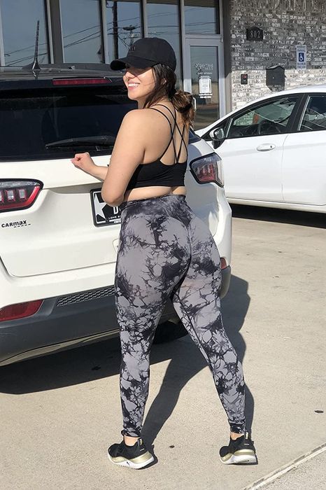 A reviewer is seen wearing black tie-dye leggings, a black sports bra, and a baseball cap.