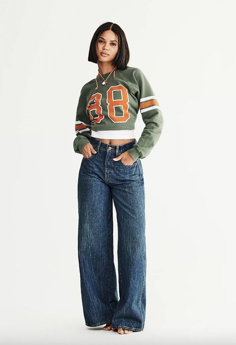 A woman in a jersey-style top and wide-leg jeans poses against a simple background.