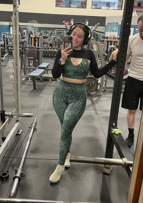 The Mytour writer is wearing a green snake skin patterned workout set paired with a black shrug and cream sneakers.