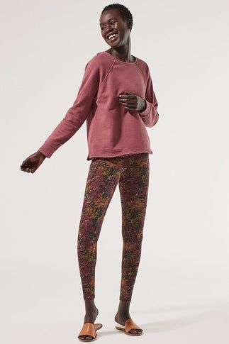 A model wearing bloom-inspired orange, purple, and green leggings paired with orange slip-on shoes