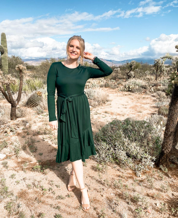 Reviewer in a green long-sleeved midi dress with a tie-string waist.