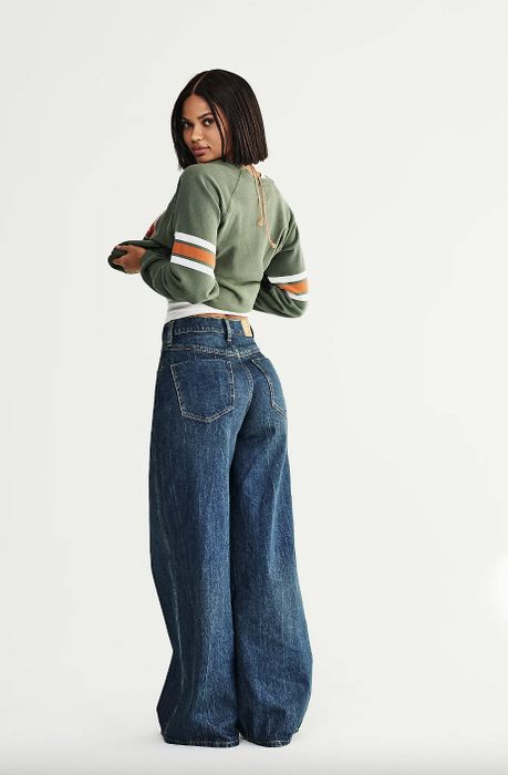 A woman in a green striped sweater and wide-leg jeans, facing away and turning her head towards the camera.