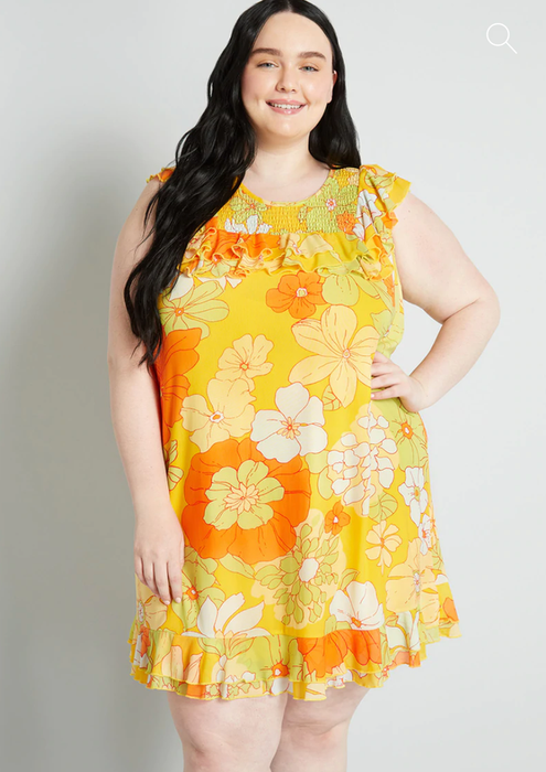 Model wearing a sleeveless floral print mini dress in vibrant yellow and orange hues.