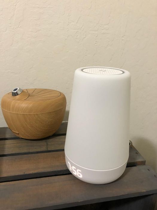 A white air purifier and a brown wooden essential oil diffuser rest on a wooden surface, with the air purifier showing a digital time display.