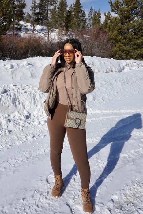 A reviewer is photographed in brown leggings, a tan top, and a matching coat, standing in a snowy setting.