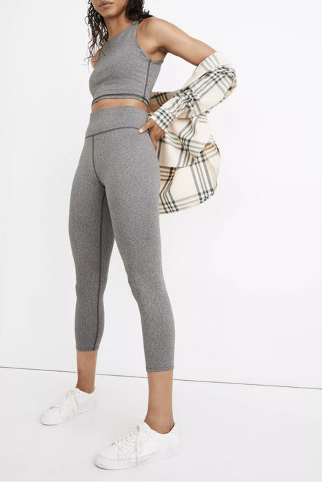 A model showcasing heather gray high-waisted leggings paired with white tennis shoes and a cream flannel shirt