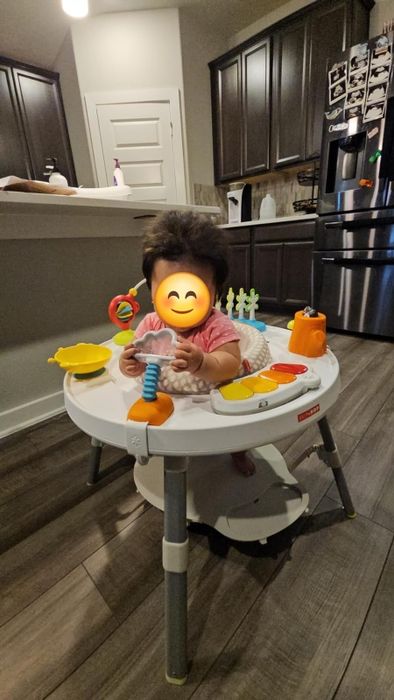 A baby enjoys playing in an activity center set up in a kitchen, interacting with a coiled toy.