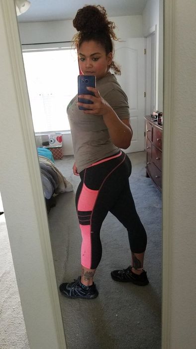 A reviewer is wearing calf-length leggings with a pink stripe down the side, featuring a pocket in the middle of the stripe.