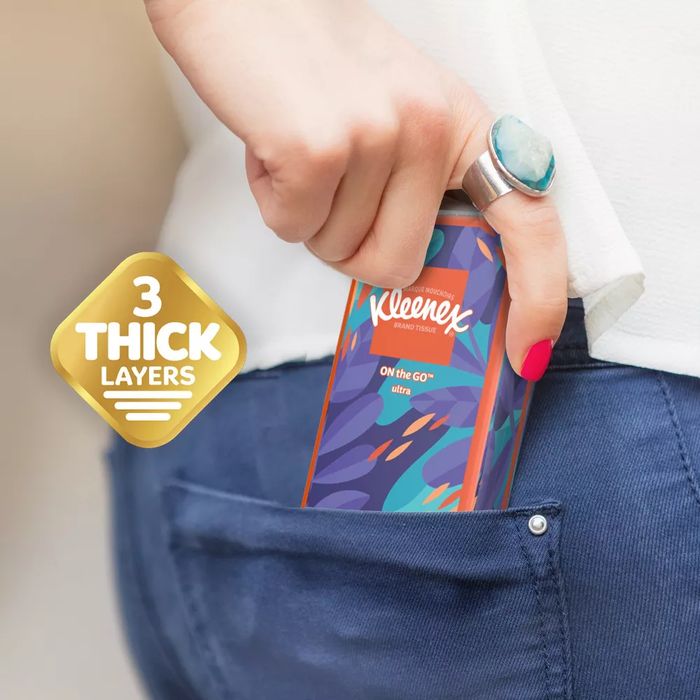A person sliding a pack of Kleenex tissues into their pocket, with the packaging labeled