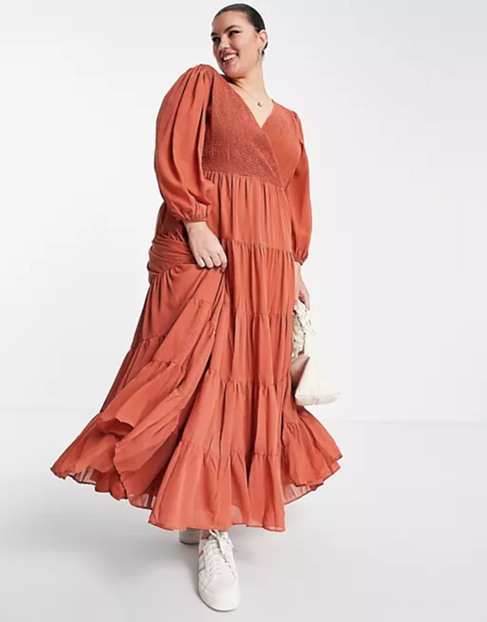 A model dons a long-sleeved rust-colored tiered maxi dress with a V-neck wrap design.