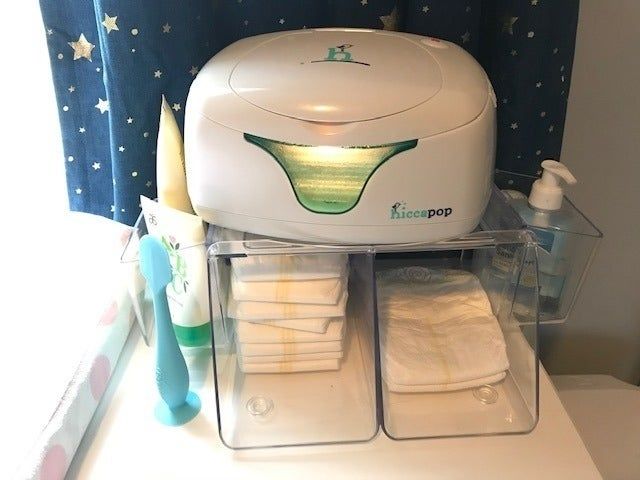 A diaper changing station complete with a wipe warmer, stocked with fresh diapers and various baby skin care products.