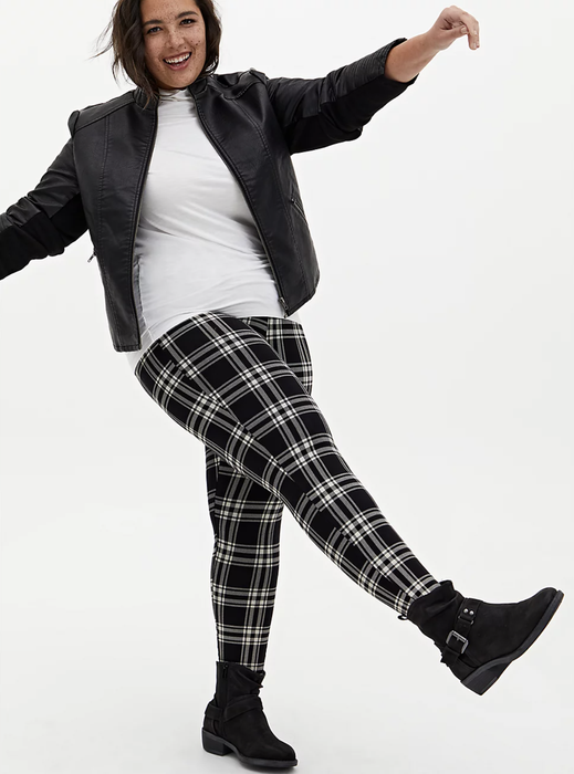 A model is styled in black and white gingham-patterned leggings, paired with a sleek leather jacket and a crisp white shirt.