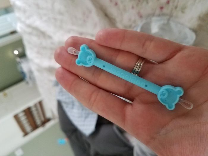 A hand grips a blue Silicon Baby pacifier clip with bear-shaped ends.