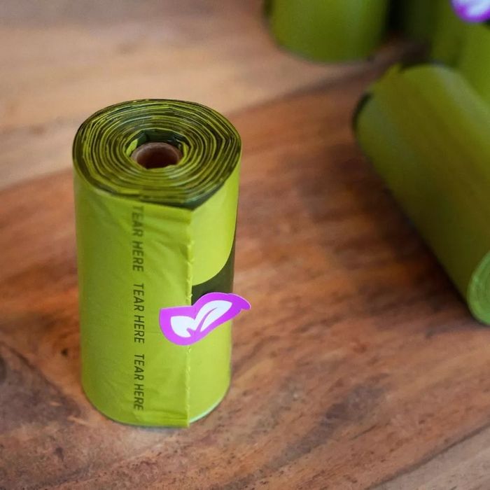 A roll of green dog poop bags standing upright on a table next to other rolls