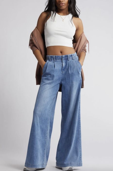 A woman in a white crop top and wide-leg jeans, casually holding a jacket over her shoulder.