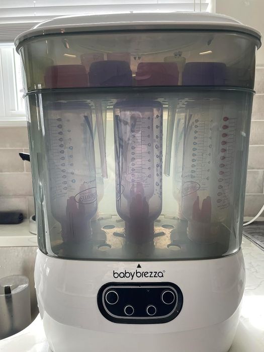 The Baby Brezza appliance holds six bottles inside its clear chamber, neatly placed on a kitchen counter.