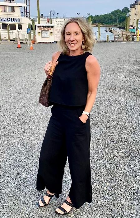 A reviewer is wearing a black pants set with a black sleeveless shirt.
