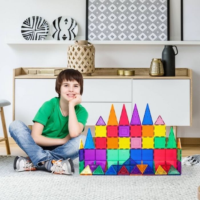 A child sits beside a castle made from magnetic tiles