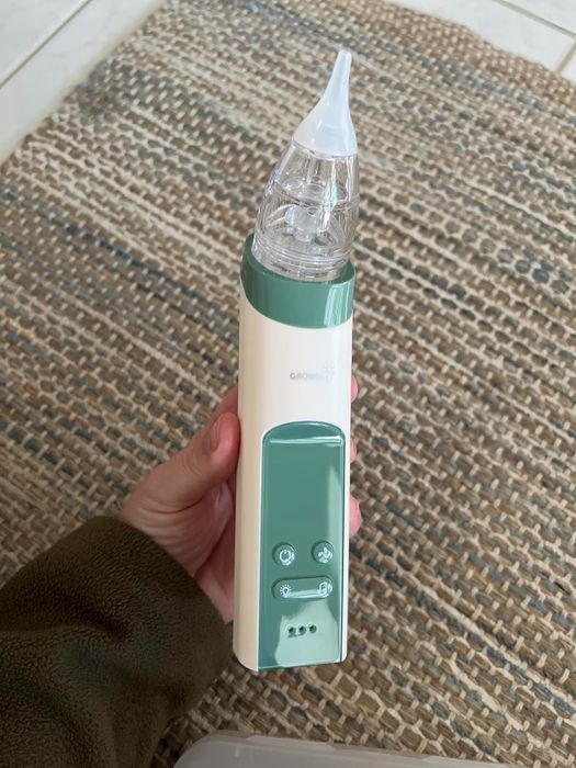A hand holds the Graco Nasal Aspirator, a device designed to safely clear your baby’s nasal passages electronically.