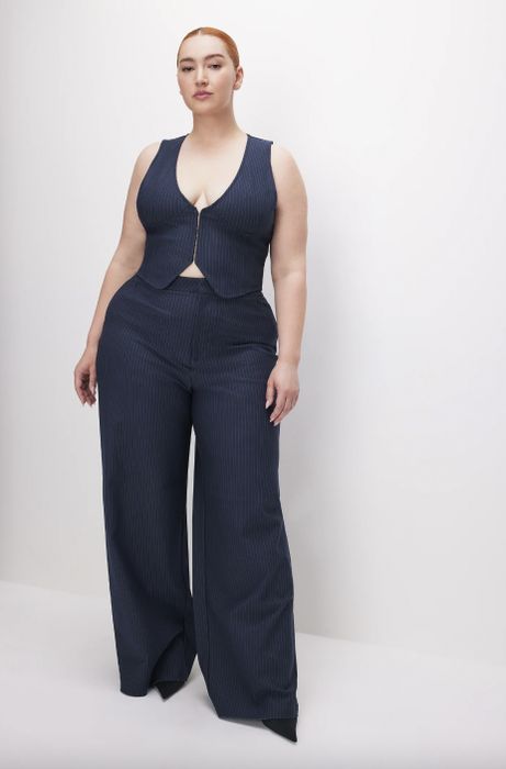 A woman strikes a confident pose in a pinstripe jumpsuit, hands placed stylishly on her hips.