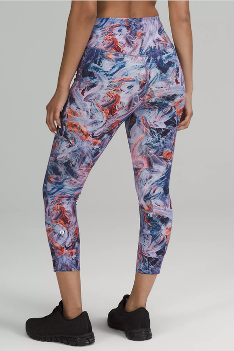 A model displaying the back view of cropped leggings with an atmospheric design, styled with black sneakers