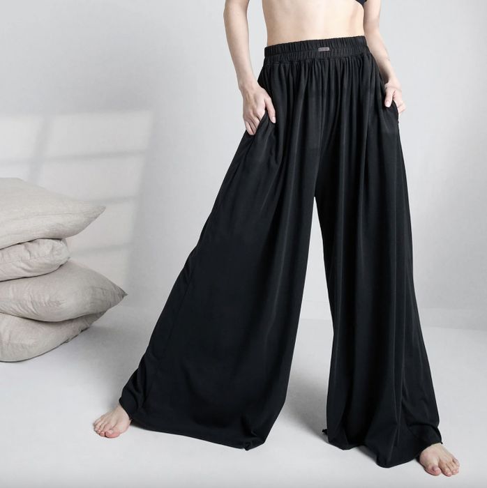 A person rocks oversized black pants with a shirred waistband, standing barefoot against a simple, neutral background.