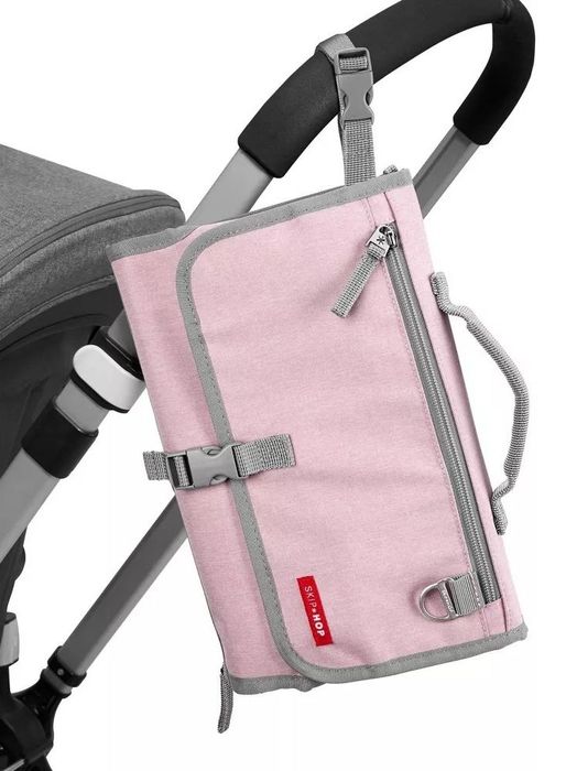 A pink diaper clutch with gray accents, folded and attached to a stroller handle