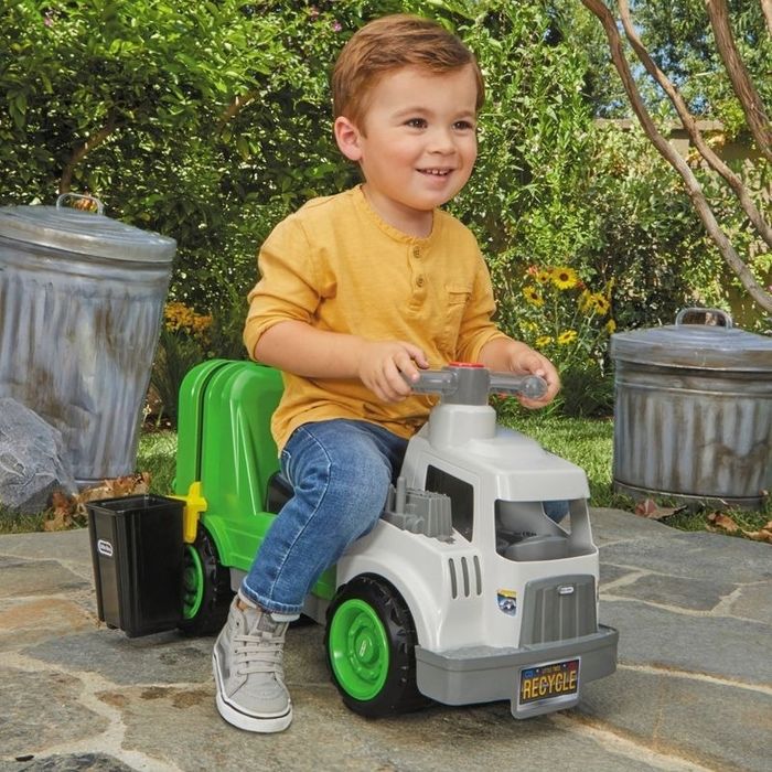A child enjoys riding a toy trash truck around the yard