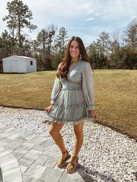 Reviewer wearing a tiered, ruffled long-sleeved white and green floral V-neck dress.