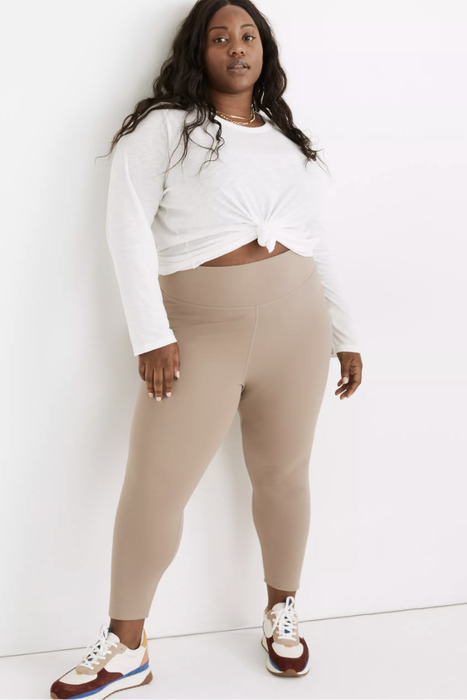 A model wearing tan leggings styled with a knotted white long-sleeve shirt and high-top sneakers