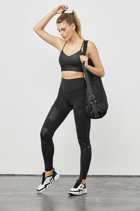 A model showcasing black moto leggings styled with black and white sneakers and a coordinating sports bra