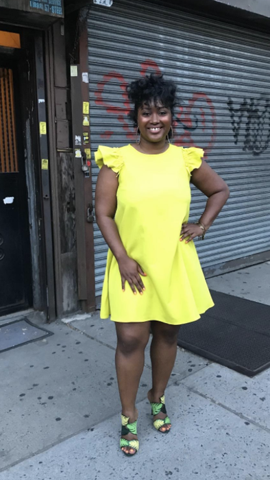 Reviewer in a bright yellow above-the-knee dress with fluttery cap sleeves