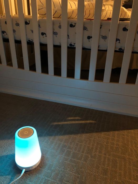 A soft-lit nursery features a crib with whale-patterned bedding, and a glowing nightlight sits on the carpeted floor below.
