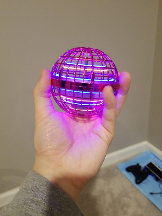 A hand holds a small, glowing orb ball, casting a soft purple light.