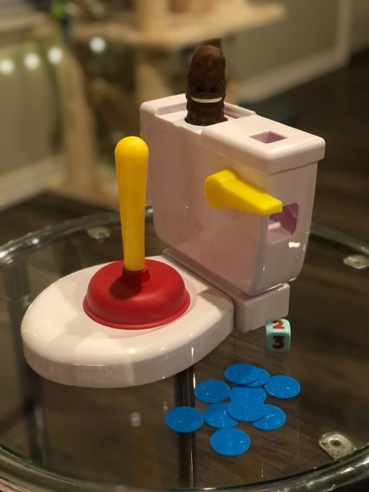 The toy toilet with a plunger, plastic poop, blue tokens, and a dice for the game