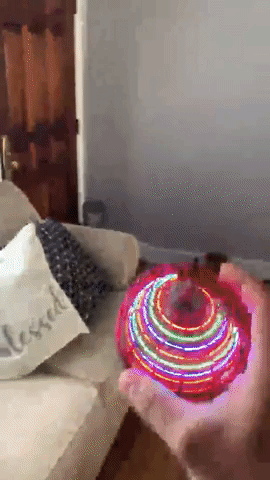 A GIF of a person tossing a spinning, light-up orb in a living room. The toy features vibrant LED lights that create mesmerizing circular patterns.