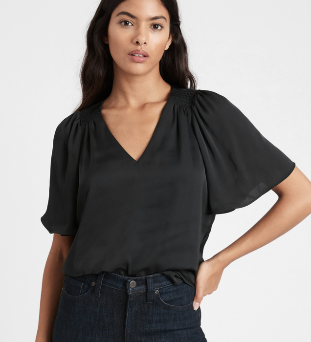 The model is wearing a satin flutter-sleeve top in black.