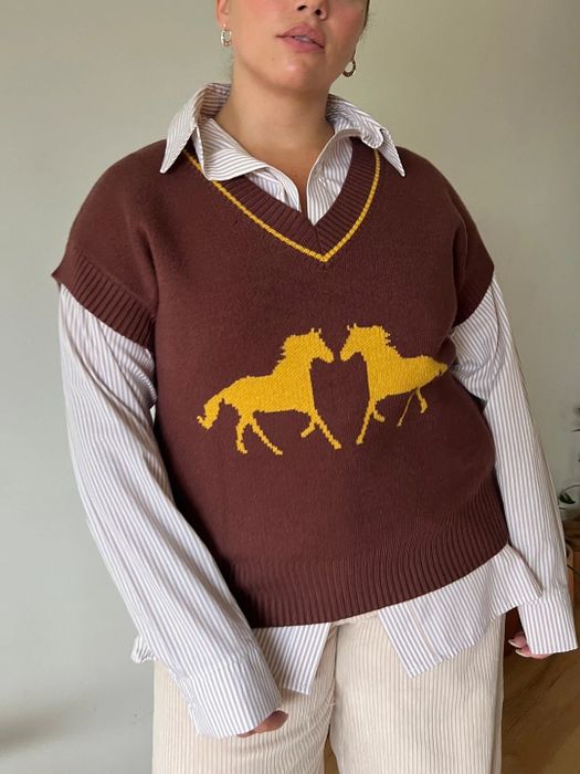 A model is wearing a brown sweater vest adorned with yellow horses.
