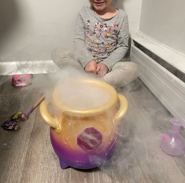 A child sitting beside a toy cauldron with smoke rising from it