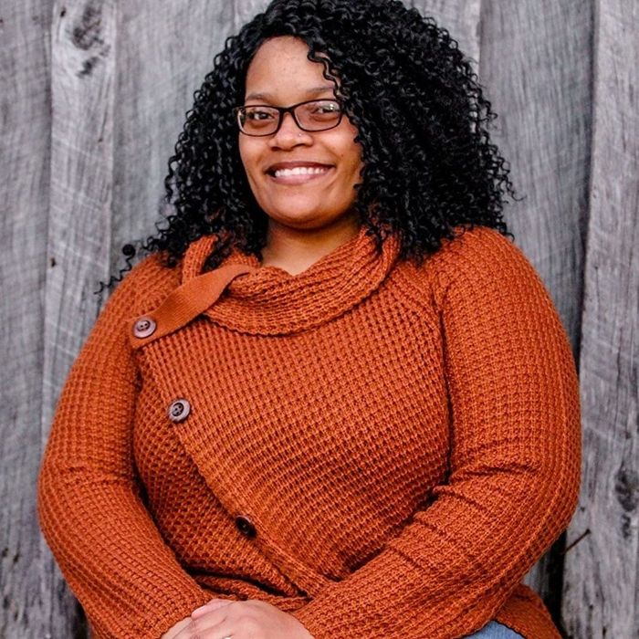 The reviewer is sporting the burnt orange asymmetrical wrap sweater paired with denim jeans.