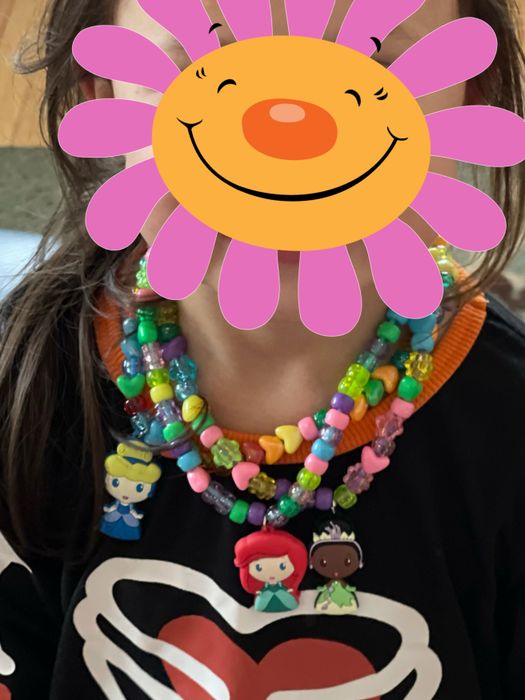 A reviewer's child wearing three colorful Disney princess necklaces they designed, proudly showing off their creations.