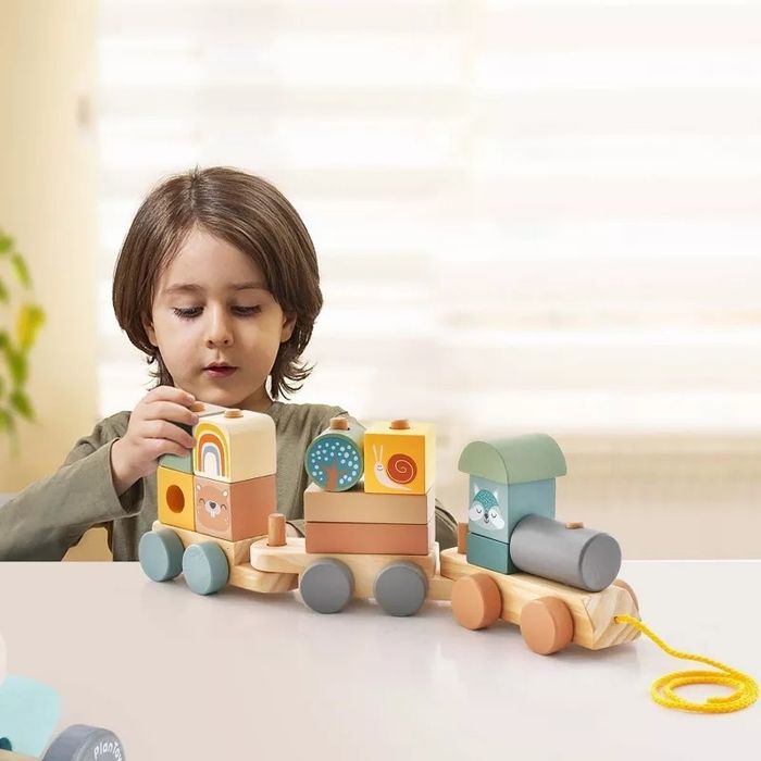 A child enjoying playtime with a wooden toy train set, complete with animal and shape blocks. The train is connected by a bright yellow string.