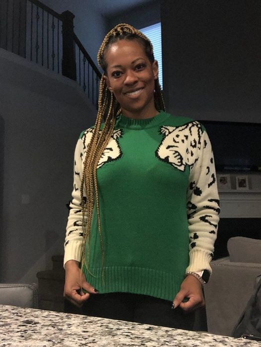 A reviewer is wearing a green sweater featuring white leopards on the sleeves of each arm.