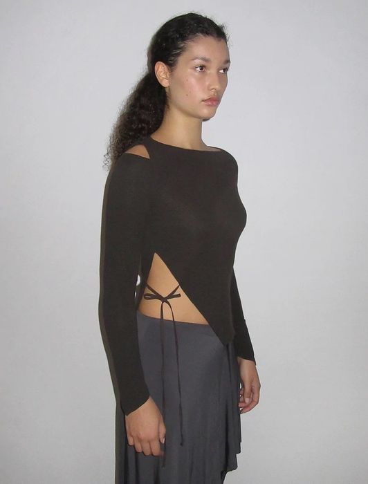 A model is wearing a brown sweater featuring a triangle cutout along the side hem, with a tie connecting the two sides.