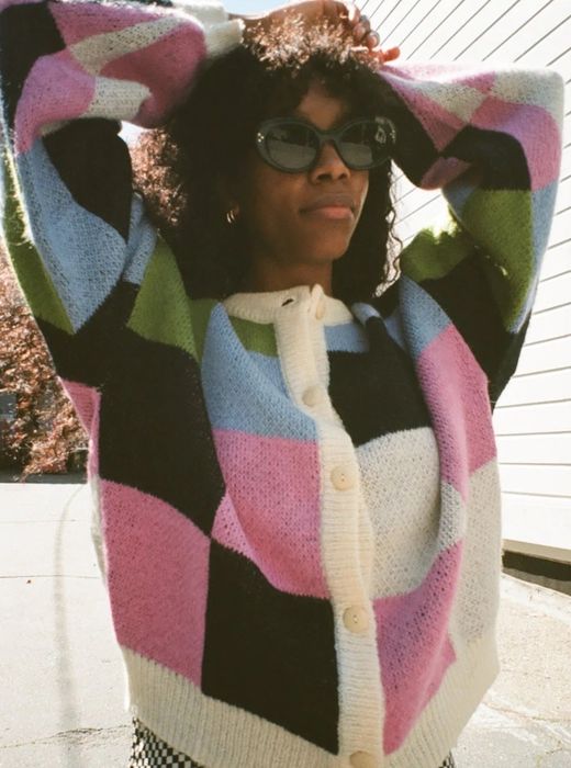 A model wearing a checkered cardigan in black, white, pink, blue, and green.